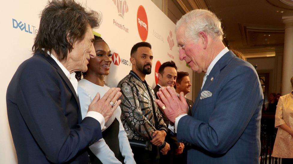 Принц Чарльз, принц Уэльский использует жест Намасте, чтобы поприветствовать Rolling Stone Ронни Вуда, когда он посещает Prince's Trust And TK Maxx