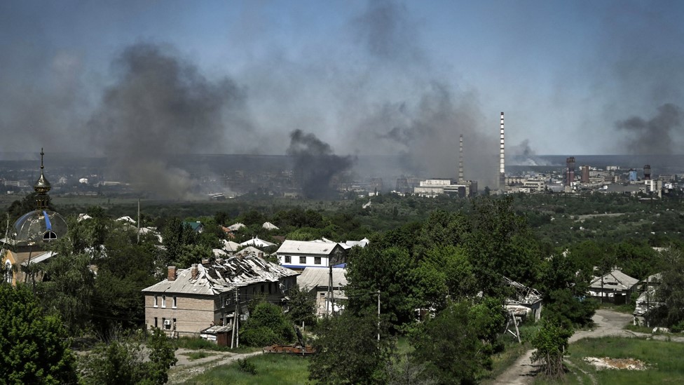 A damaged building can be seen in Lysychansk as black smoke rises from the nearby city of Severodonetsk