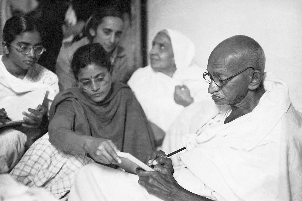 Gandhi escribiendo mensaje con ayuda de Abha y Manu, tras interrumpir su ayuno, Nueva Delhi, India, 1948.