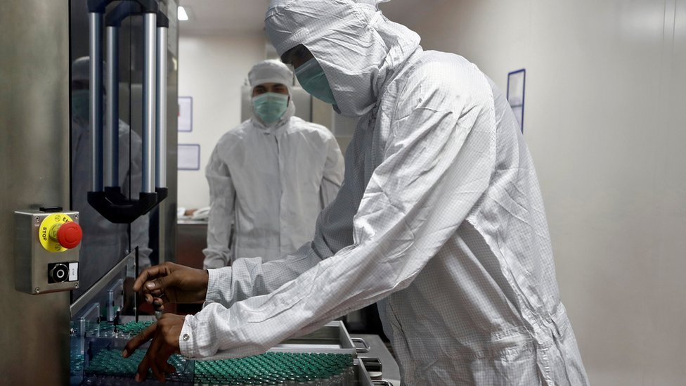A man in PPE is working with vaccine vials in a factory