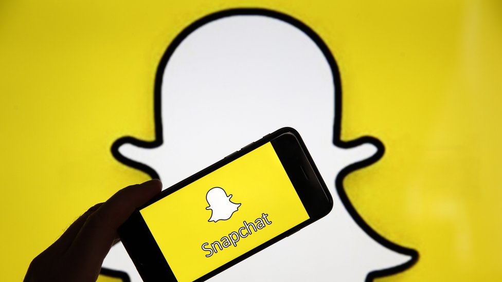 Логотип-призрак Snapchat выглядит как фон с телефоном и приложением, установленным перед ним