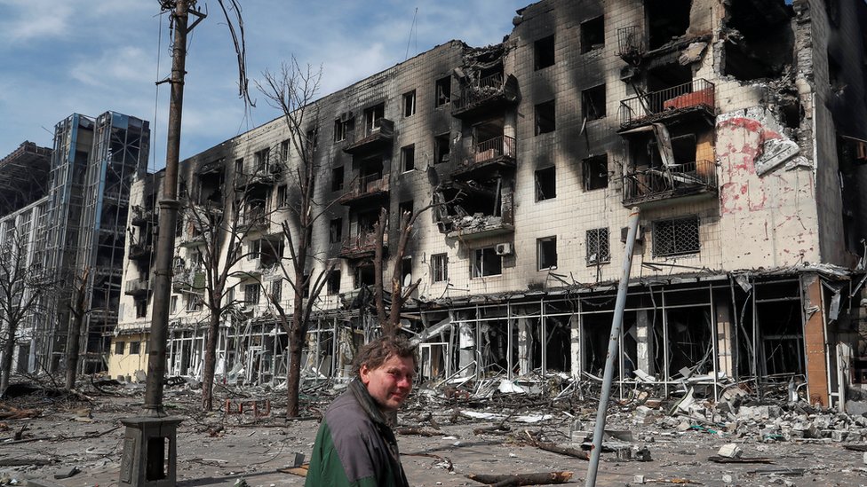 A man stands in front of a destroyed residential building in Mariupol