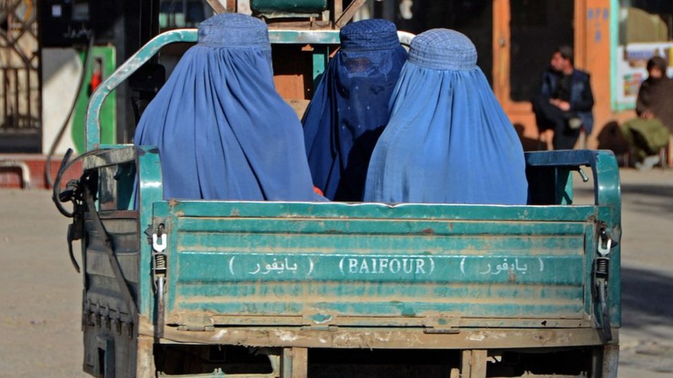 Perempuan yang mengenakan burqa bepergian di atas mobil bak terbuka di jalanan kota Kandahar.