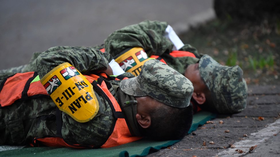 Militares descansan en plena calle tras horas de trabajo de rescate. Rescatistas se toman un tiempo para descansar tras horas de trabajo.