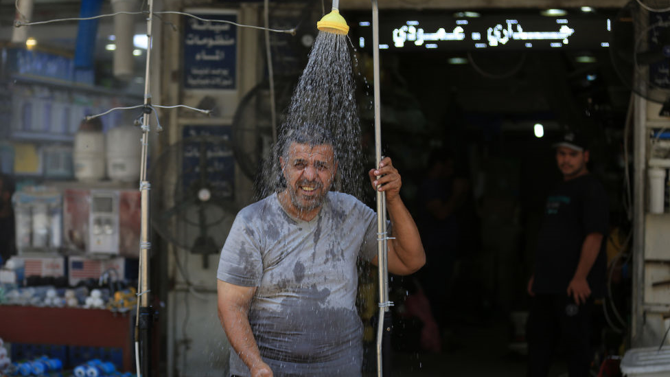A man cools off under a roadside shower as temperatures exceed 45C in the capital city Baghdad, Iraq