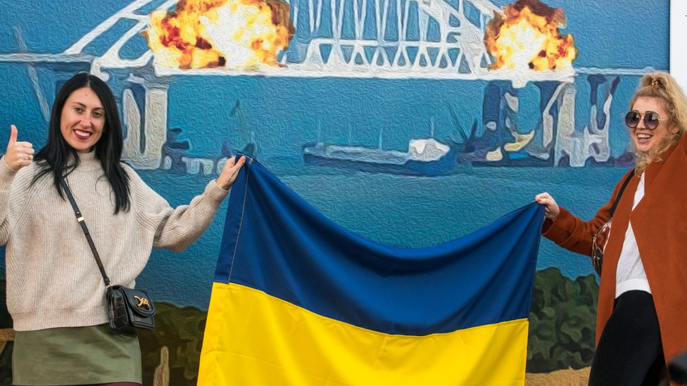 Two women pose with the Ukrainian flag in front of the artwork in central Kyiv, Ukraine