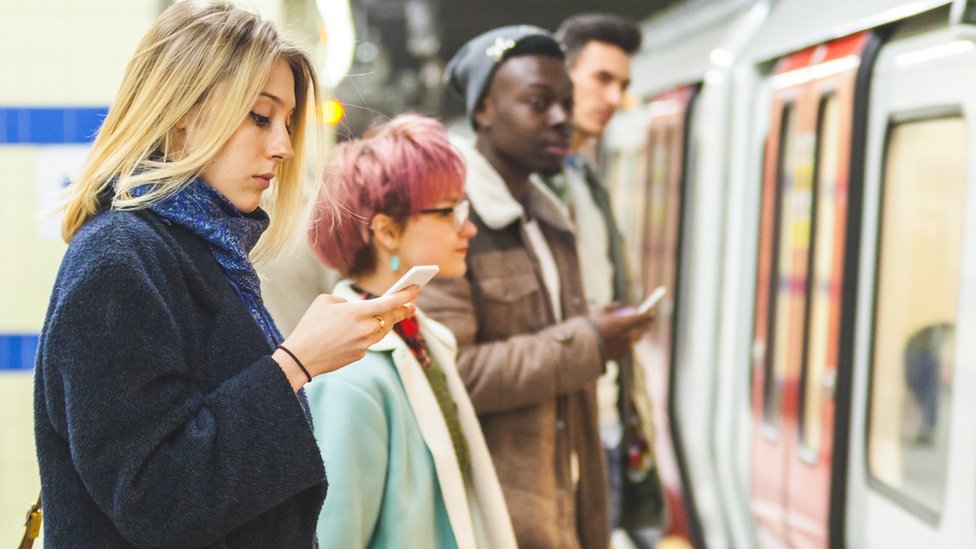 Женщина смотрит в свой телефон на платформе трубки в Лондоне