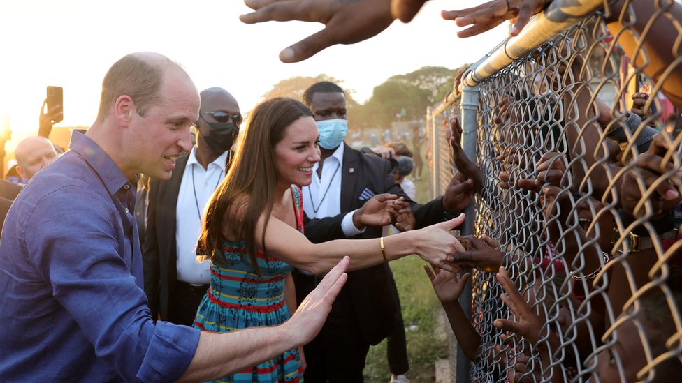 El duque y la duquesa de Cambridge saludan a niños a través de una reja en Kingston, Jamaica