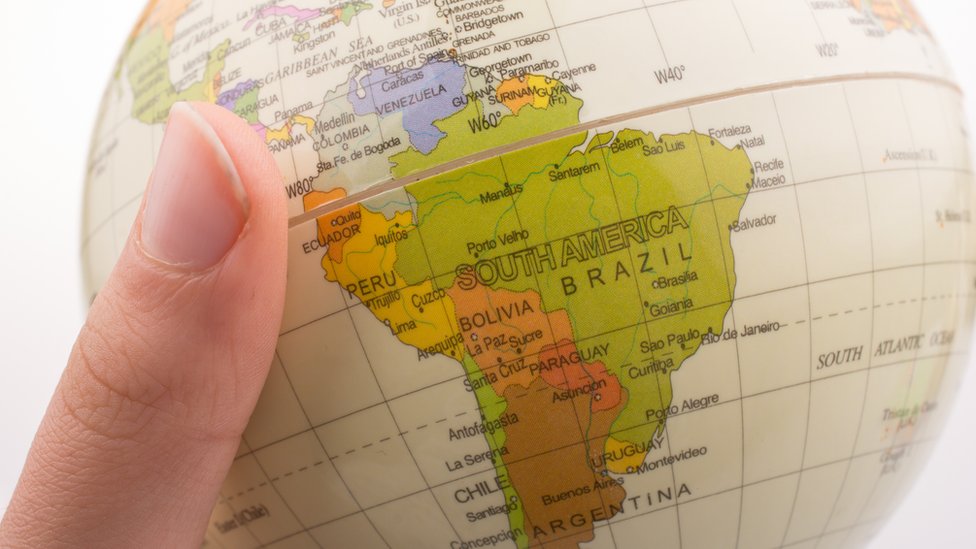 Mano de mujer agarrando globo terráqueo con el mapa de Sudamérica.
