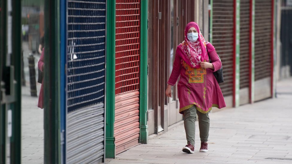 Женщина в маске проходит мимо закрытых магазинов Кардиффа