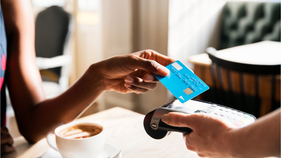 Mão de mulher aproximando um cartão de crédito de uma máquina de pagamentos