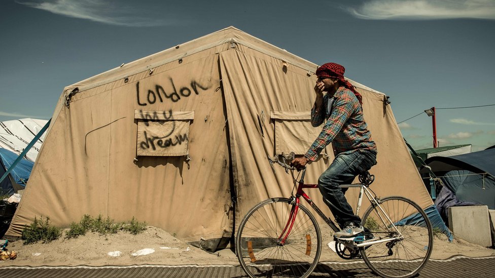 На этой файловой фотографии, сделанной 24 июня 2016 года, изображен мигрант, едущий на велосипеде в лагере для мигрантов и беженцев «Джунгли» в Кале, на следующий день после того, как Великобритания проголосовала за выход из ЕС.