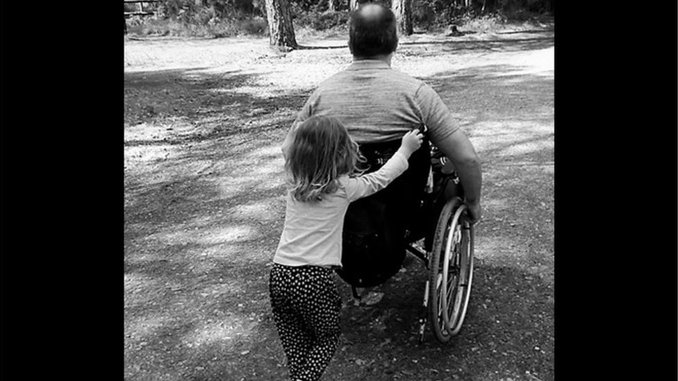 Ian Taverner with one of his daughters pushing him in a wheelchair