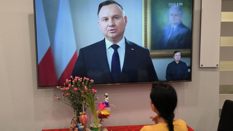 Женщина наблюдает за тем, как президент Польши Анджей Дуда выступает на экране телевизора 10 апреля по случаю годовщины гибели президента Леха Качиньского в авиакатастрофе