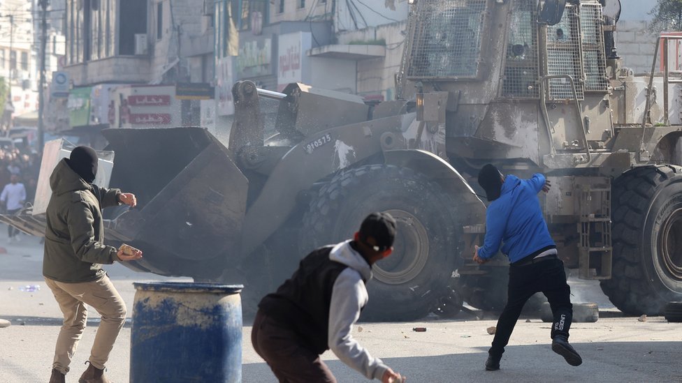 Three men throwing stones at armoured vehicle