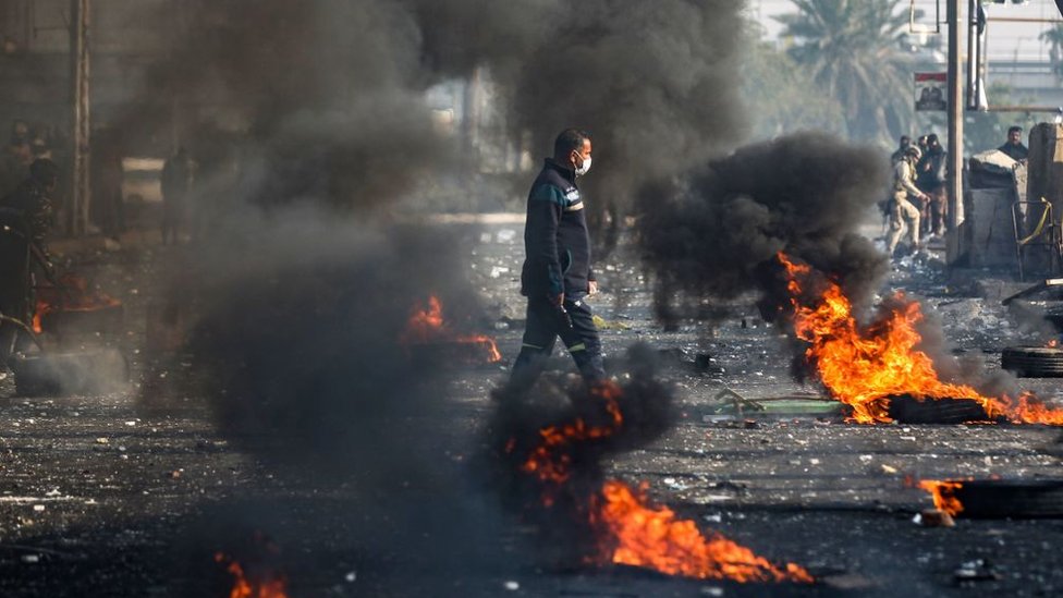 متظاهر في بغداد يمشي بين إطارات السيارات المشتعلة