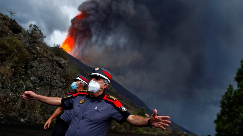 Policemen with the eruption of the volcano behind.