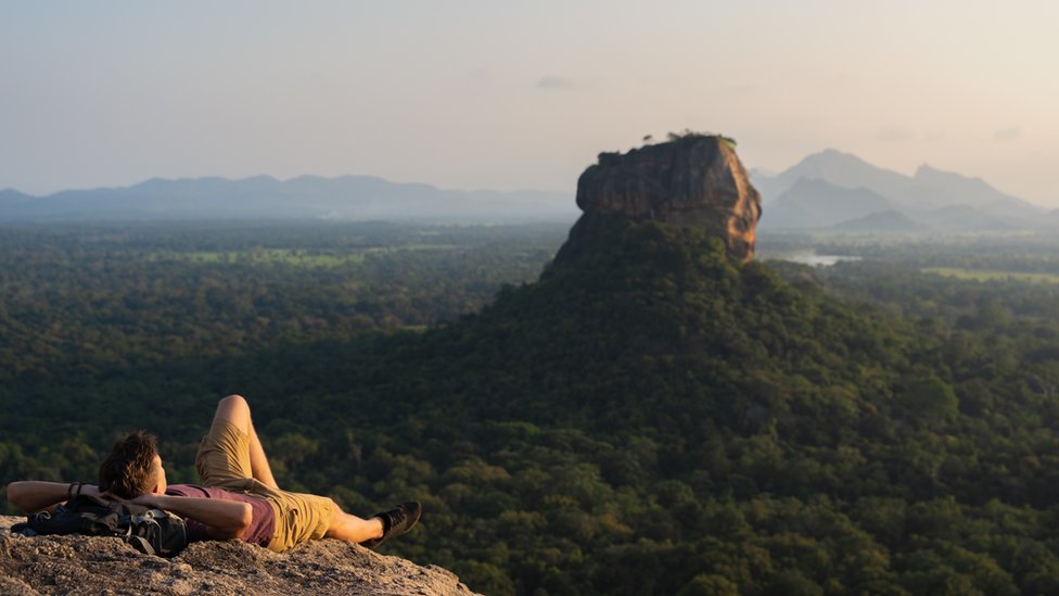 Um turista deitado, olhando para Lion Rock em um vale de árvores