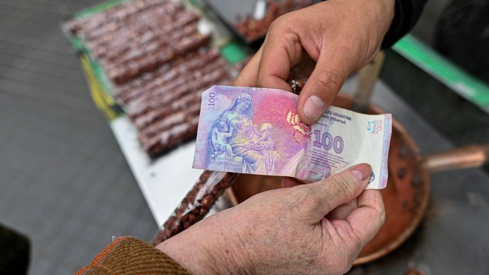 Dos mujeres intercambian un billete de 100 pesos argentinos