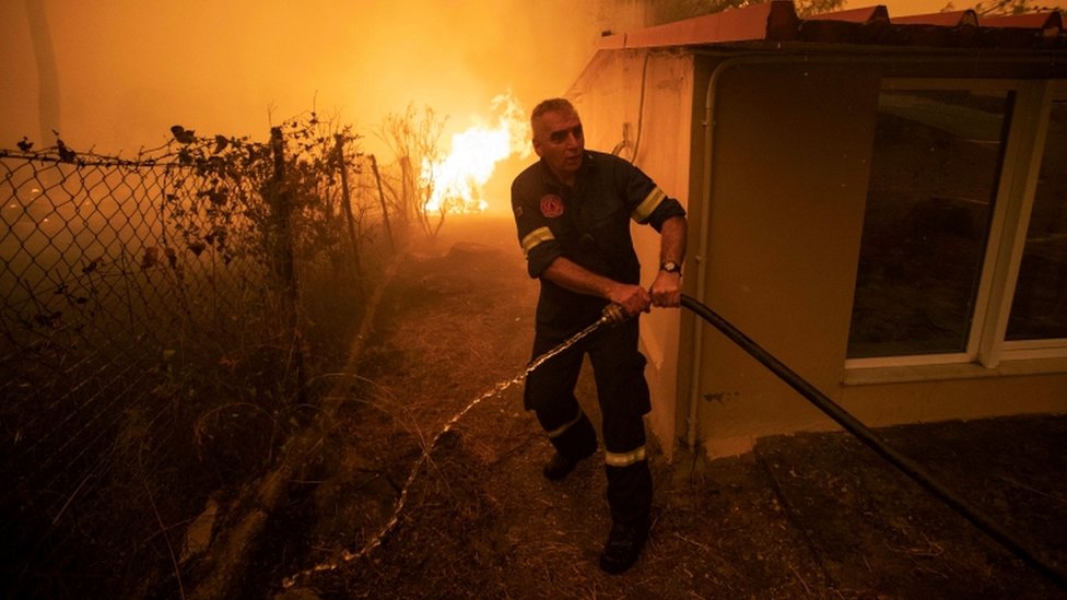 Un bombero intenta acerca una manguera para sofocar un incendio en una casa de la isla griega Evia.