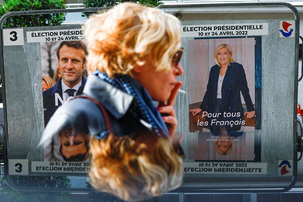 امرأة تسير أمام ملصقات الحملة الرسمية لمرشحي الانتخابات الرئاسية الرئيس إيمانويل ماكرون ومارين لوبان في باريس ، في 19 أبريل/نيسان 2022
