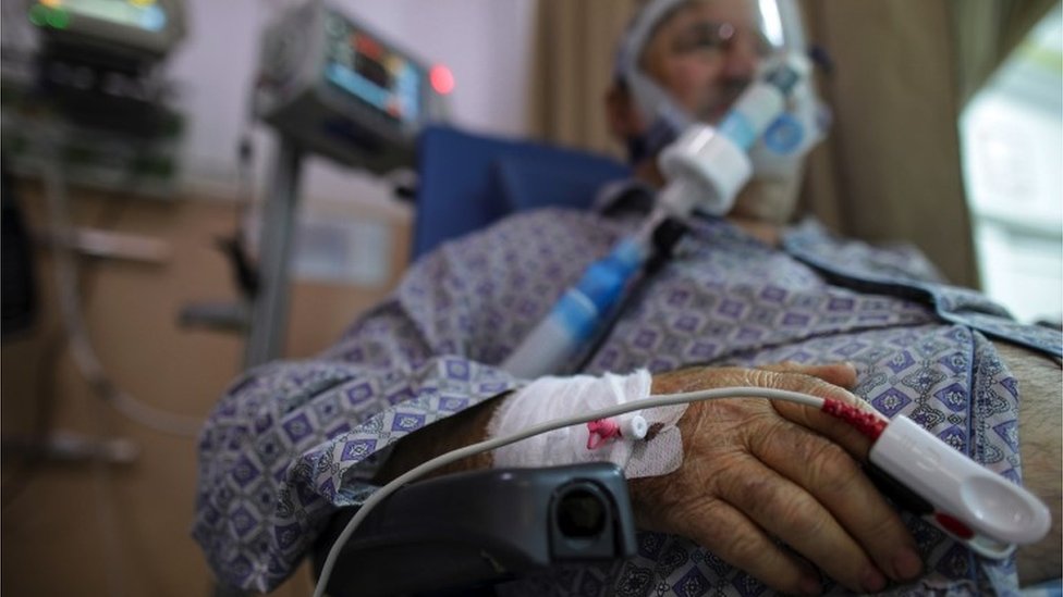 A patient sits in a wheelchair while receiving oxygen through a mask in a COVID-19 ER unit