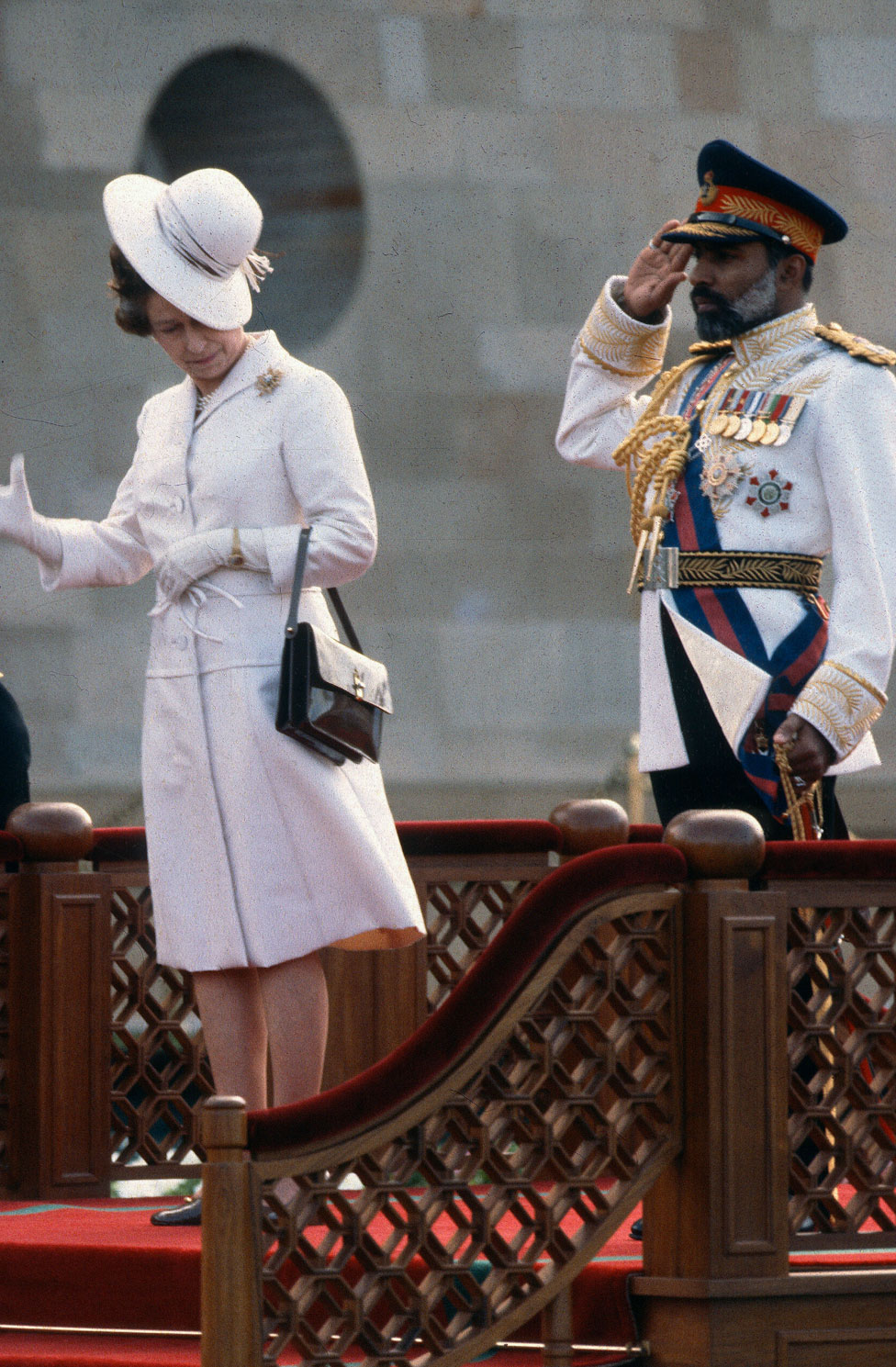 Queen Elizabeth ll nearly loses her hat in the wind as she attends a welcoming ceremony with Sultan Qaboos of Oman on 28 February 1979 in Muscat. Oman.