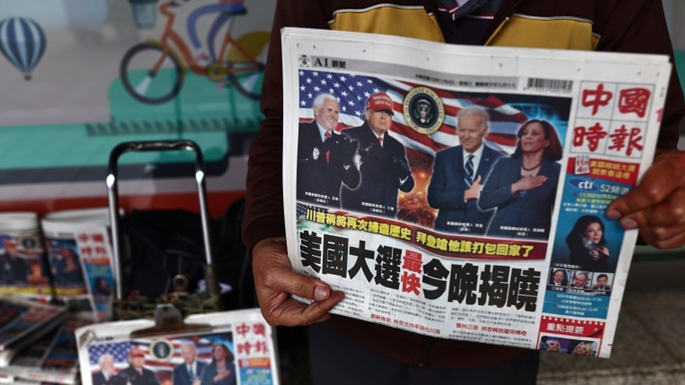 Мужчина продает газеты со статьями на первых полосах о выборах в США на одной из улиц Тайбэя