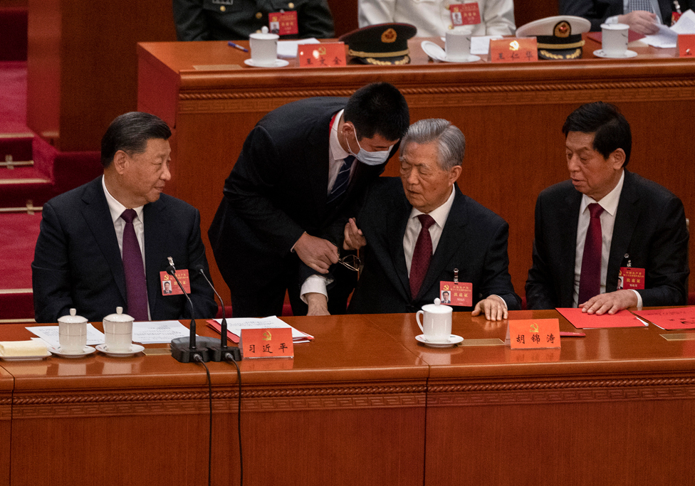 Chinese President Xi Jinping, left, Li Zhanshu, and Wang Huning, right, look on as former President Hu Jintao, centre, is escorted out of the closing session of the 20th National Congress of the Communist Party of China, in Beijing, on 22 October 2022.