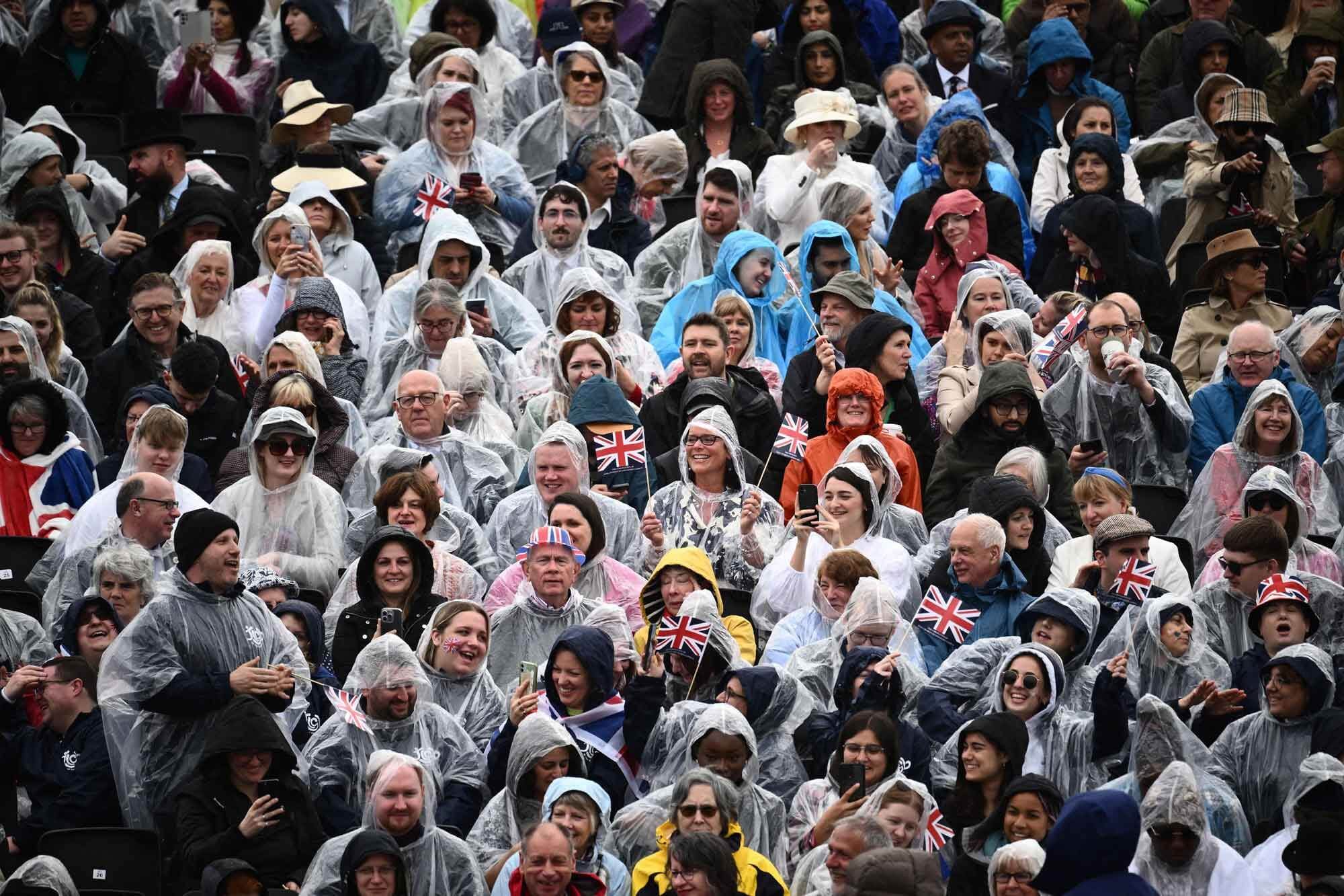 Spectators wearing waterproofs sit on stands erected along The Mall