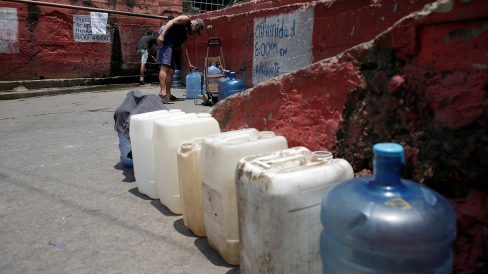 Мужчина наполняет пластиковые контейнеры водой из трубы на улице в трущобах во время общенационального карантина из-за вспышки коронавирусной болезни (COVID-19) в Каракасе, Венесуэла 2 апреля 2020 г.