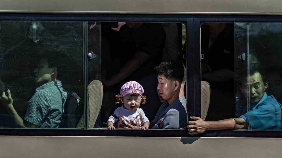Baby looking out of a Pyongyang bus while her father holds her secure