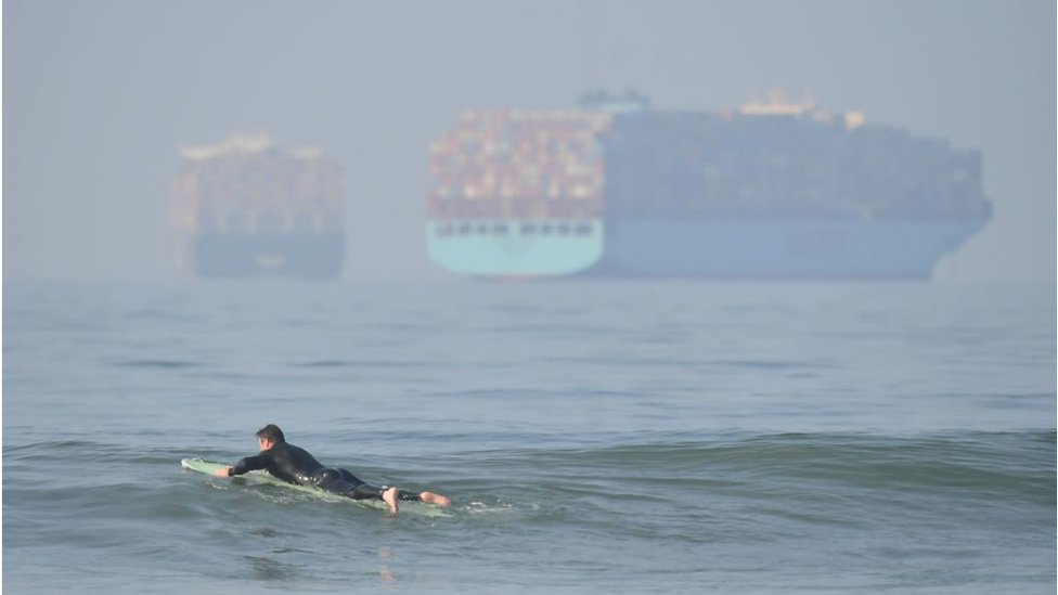 Surfista com navios porta-contêineres ao fundo