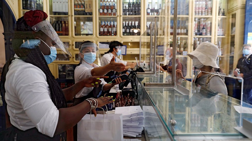 Персонал в защитных масках и масках обслуживает клиентов из-за ширм в кафе в Лиссабоне