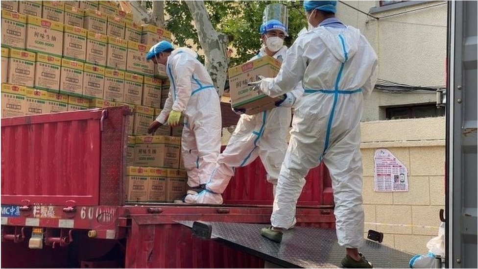 2022年4月21日，身穿防護服的人員從運往上海的卡車上卸下標有鮮味生抽的包裝箱