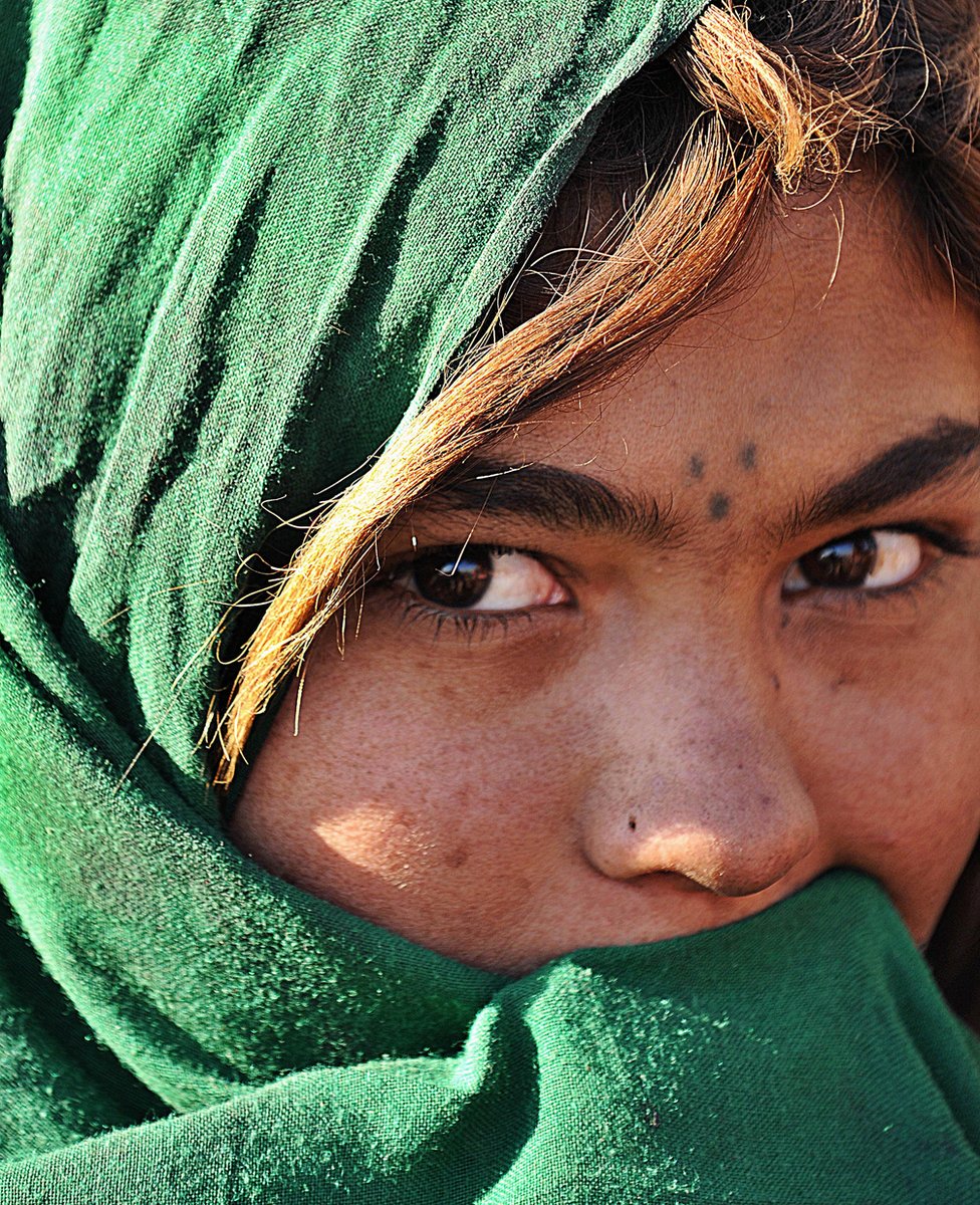 An Afghan girl from a family which returned from Iran covers her face as she stands in front of her tent on the outskirts of Kabul, February 2008