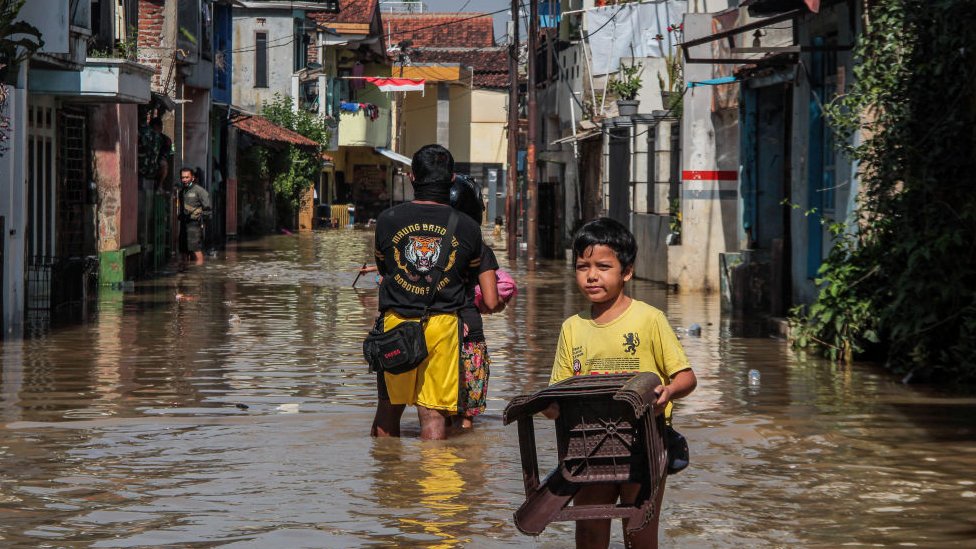 Boy carrying a chair through a flooded street