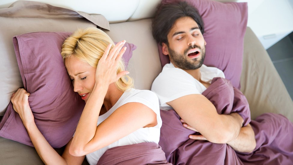 Hombre roncando con su pareja en la cama.