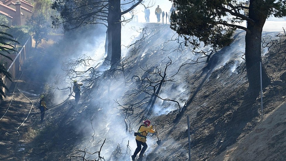 Пожарные работают на обугленном склоне холма возле домов и шоссе 118 в Сими-Вэлли, Калифорния, 30 октября 2019 г.