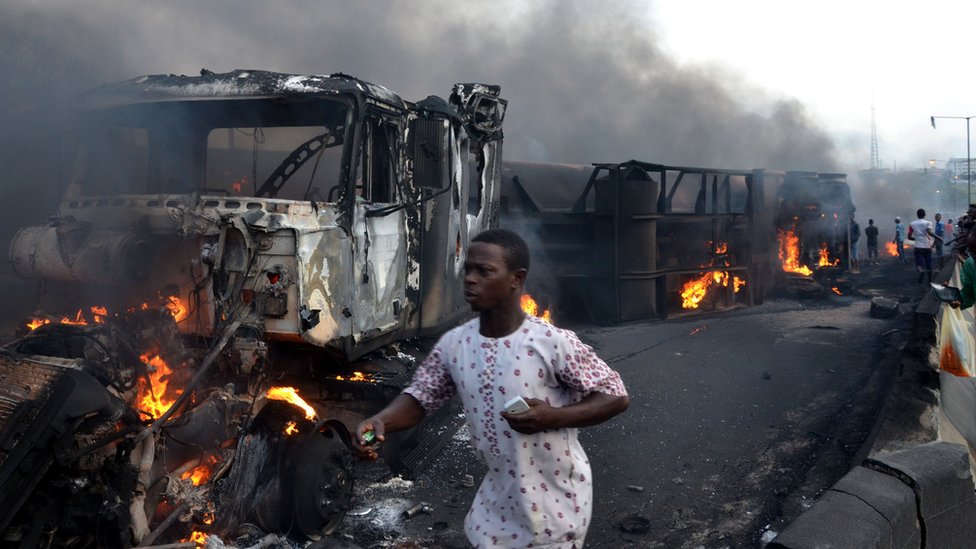 Прохожие идут среди сгоревших автомобилей после взрыва нефтяного танкера на шоссе в Лагосе, 28 июня 2018 г.