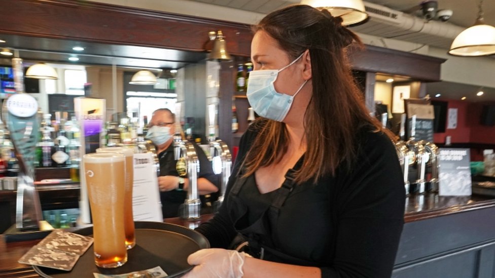 Официантка в маске держит поднос с двумя пинтами пива