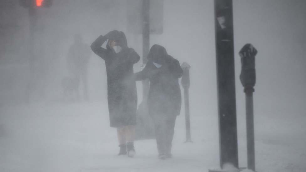 People protect themselves from blowing wind and snow during white-out conditions as Winter Storm Kenan