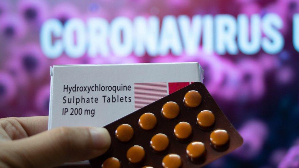 Cartela de comprimidos e caixa escrito 'hidroxicloroquina', com painel escrito 'coronavírus' atrás