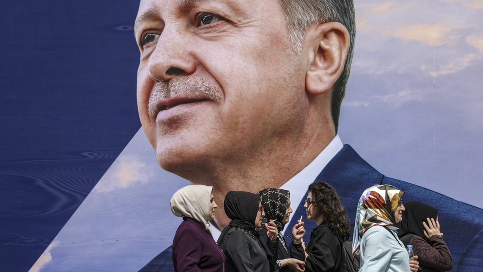 Women walk in front of an election campaign poster of Turkish President Recep Tayyip Erdogan in Istanbul