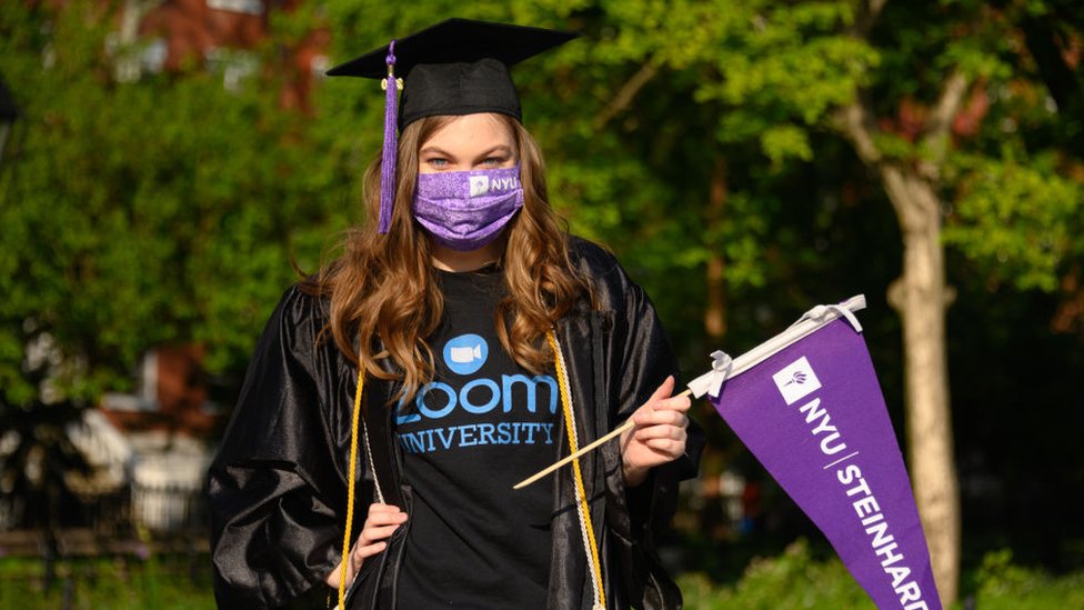 Студент носит защитную маску для лица, выпускной кепку и выпускной халат в парке Вашингтон-сквер во время пандемии коронавируса 15 мая 2020 г.