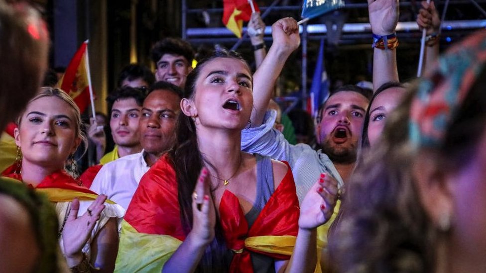 People wrapped in Spanish flags cheer in the street