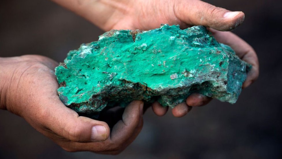 A turquois cobalt rock held in a pair of hands