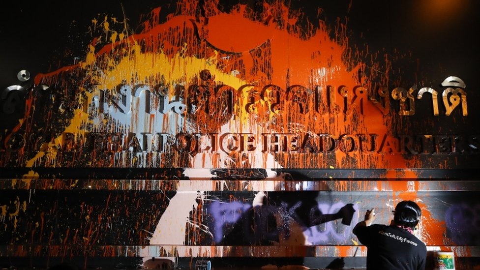 A demonstrator throws paint over a plaque with lettering on it in front of the police headquarters during a rally in Bangkok