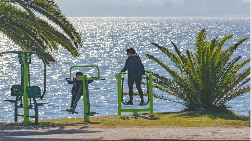 Uruguay está entre los cinco países de la región de las Américas que invierte un 6% de su PIB en salud. Una mujer y un niño haciendo ejercicio al aire libre en Punta del Este, Uruguay.