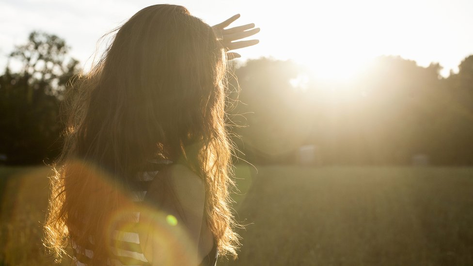 Una mujer a contraluz, tapa con la mano la intensidad de la luz del Sol